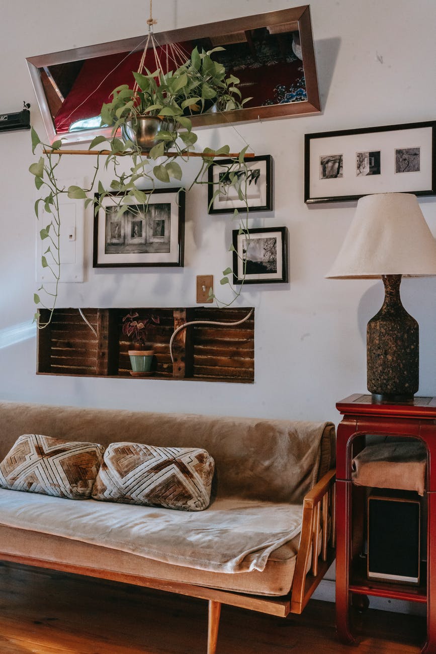 couch and small display cabinet with elegant lamp near wall decorated with framed pictures at home